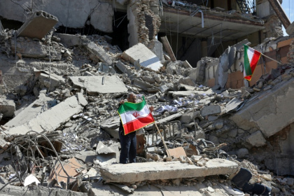 A man holds an Iranian flag amid the debris of a destroyed building following airstrikes in central Tehran - - (AFP)